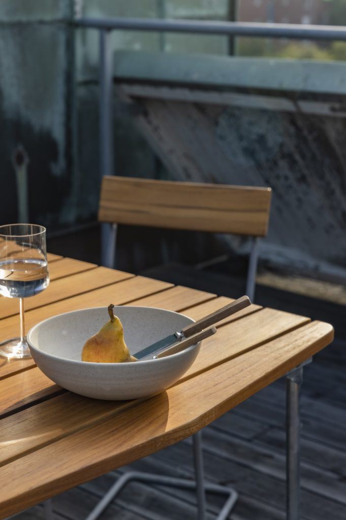 Ett gult päron ligger i en vit skål på ett teak-bord